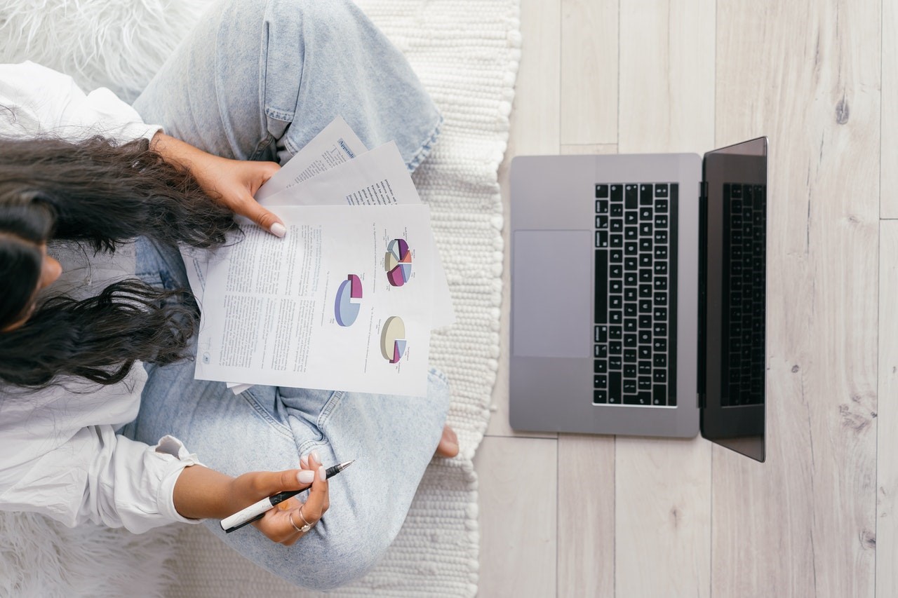 woman looking at research article seated on the floor with laptop