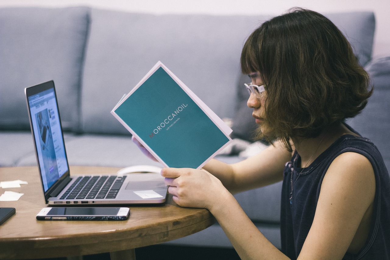 young asian woman at a computer reading a book