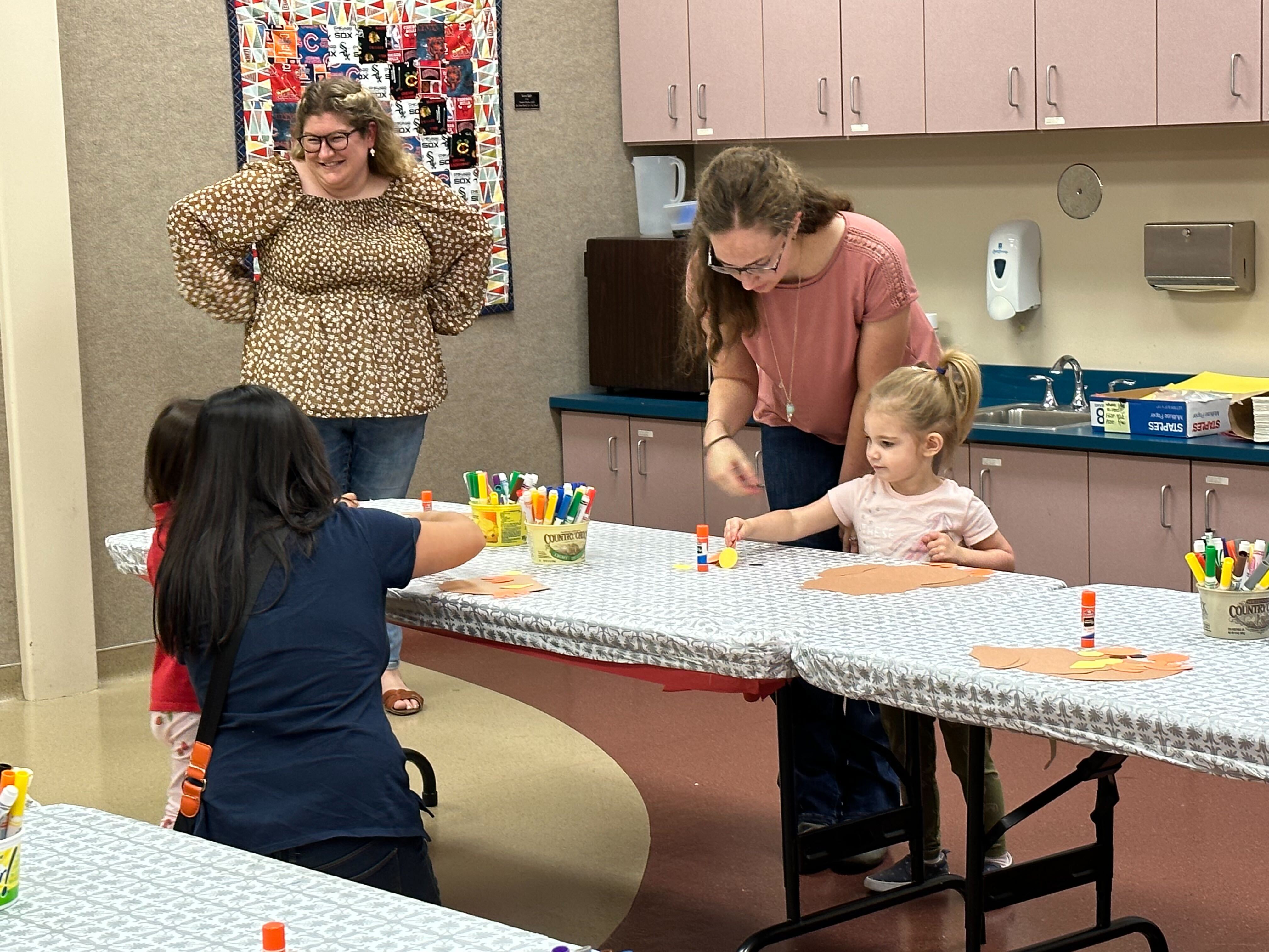 Adults and children stand around small tables doing a craft.